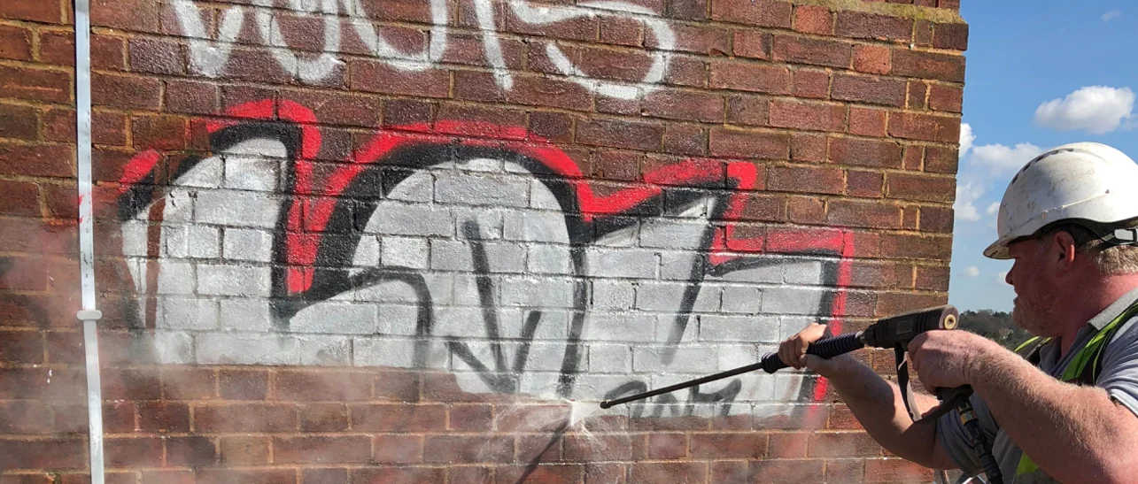 A professional using a pressure washer to remove graffiti from a brick wall.